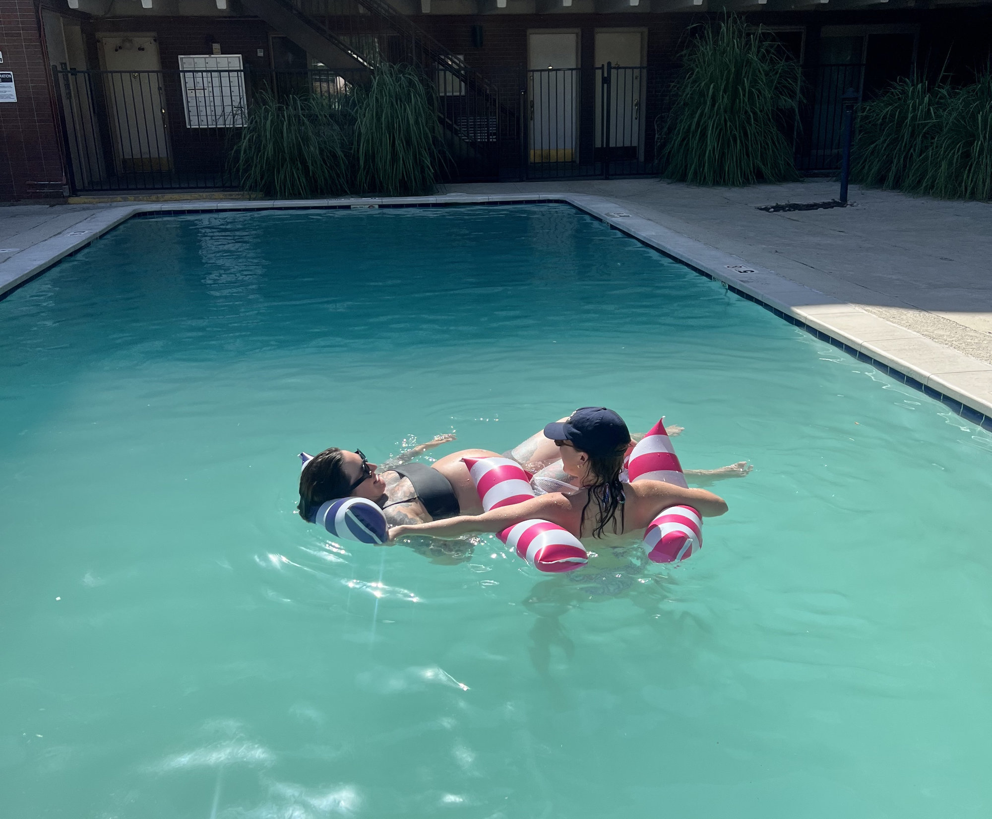 Two women lay on floaties in a pool.